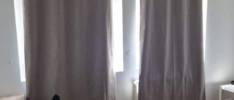 A room with a bed, a desk, and a chair. There are curtains on the windows.