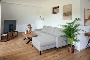 Ett vardagsrum med en grå hörnsoffa, ett soffbord i trä, en golvlampa och en krukväxt.