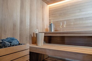 Ein Sauna-Bereich mit Holzwänden, einer Sitzbank, einem Metallbehälter mit einer Flasche und zwei Gläsern.