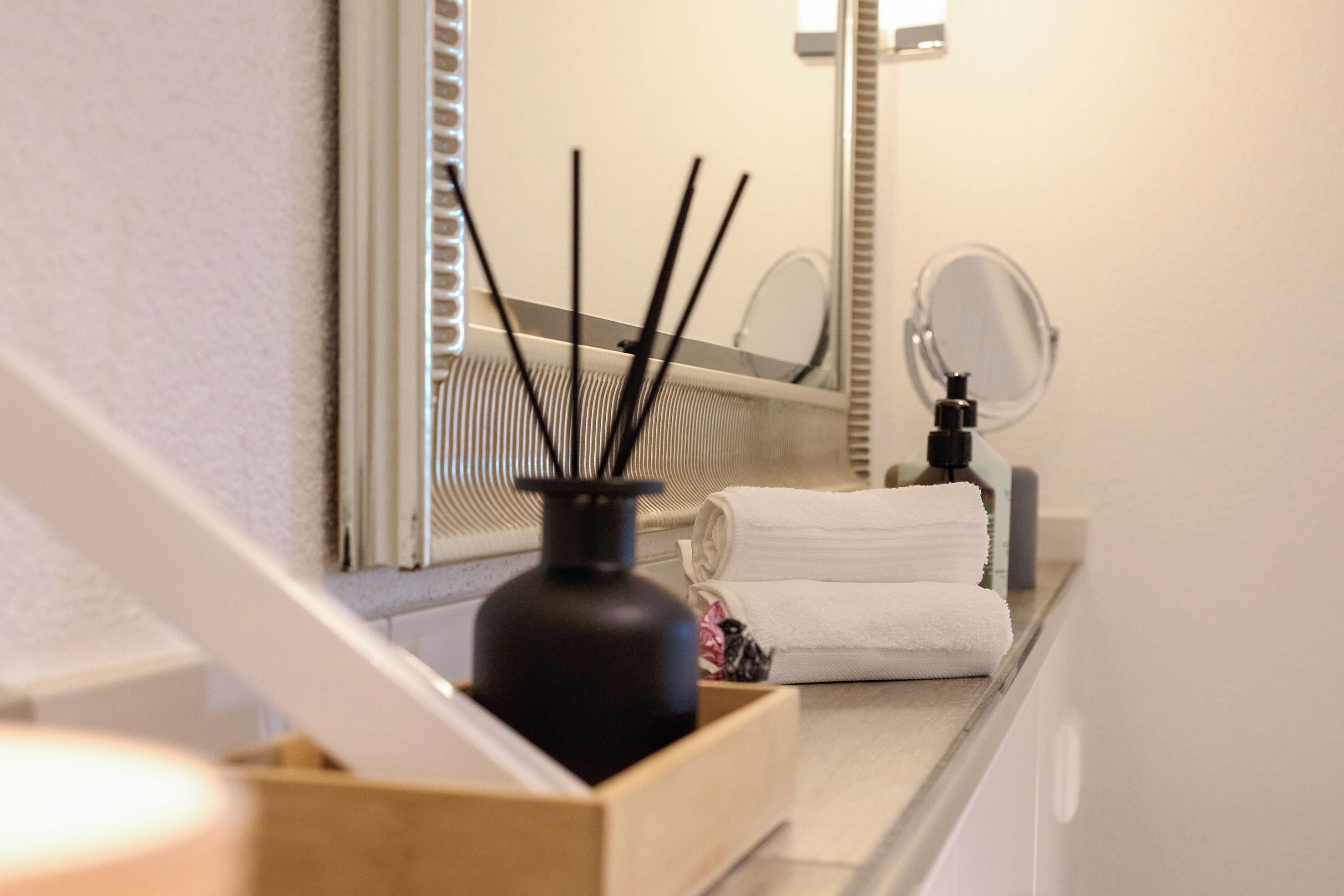 A bathroom with a mirror, a towel, and a black bottle on a counter.