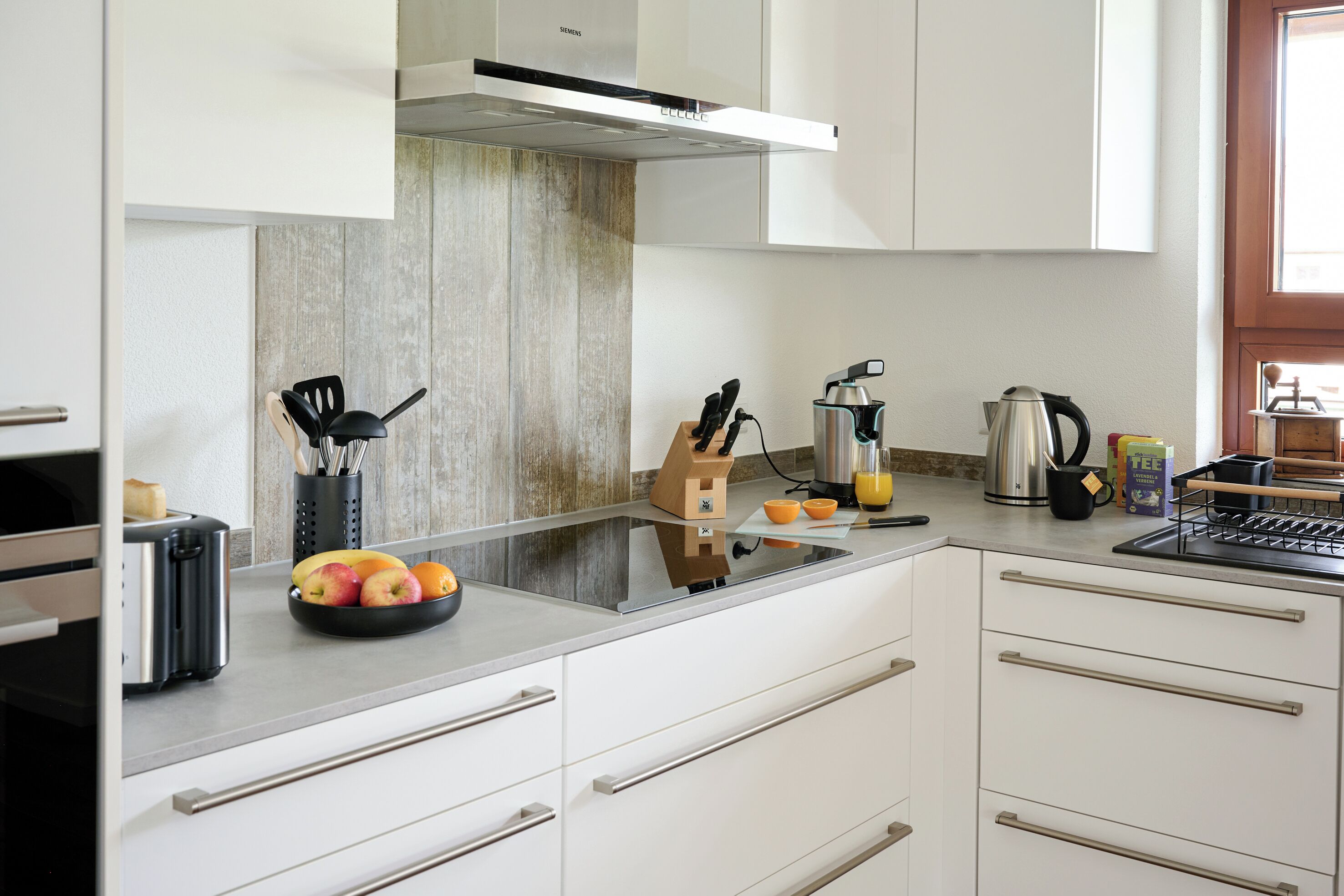 Una cocina moderna con armarios blancos, una campana extractora de acero inoxidable y un protector de cocina de madera.