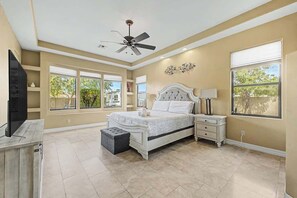 A bedroom with a bed, nightstands, a TV, a ceiling fan, and large windows. - Family Retreat • 6BR • Sleeps 13 • Parking (Phoenix)
