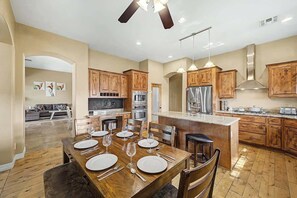 A modern kitchen with wooden cabinets, stainless steel appliances, and a dining area with a wooden table set for four. - Family Retreat • 6BR • Sleeps 13 • Parking (Phoenix)
