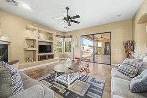 A living room with a TV, fireplace, ceiling fan, and a dining area with chairs and a table. - Family Retreat • 6BR • Sleeps 13 • Parking (Phoenix)