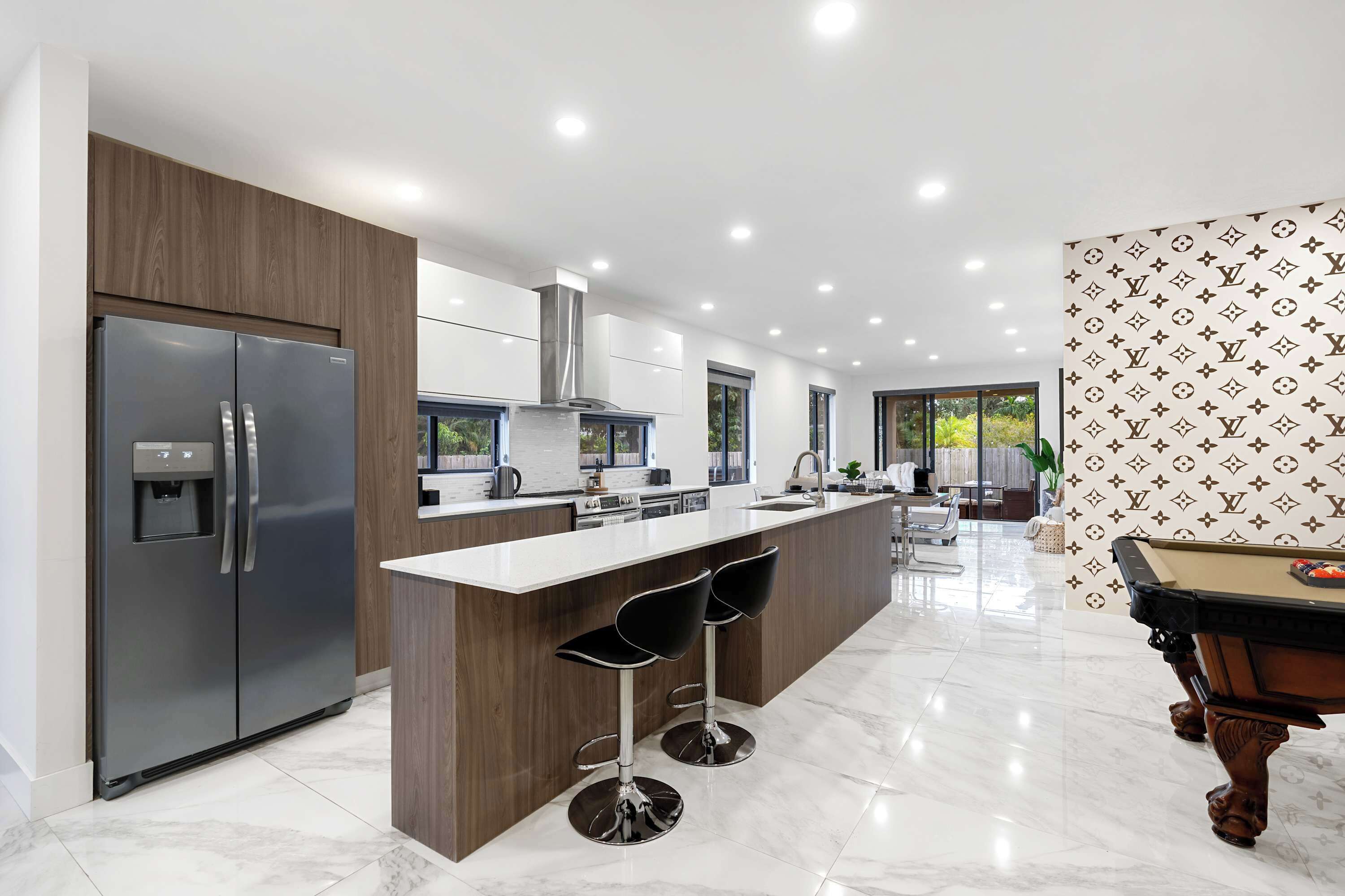 A modern kitchen with a central island, stainless steel appliances, and a pool table.