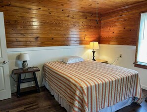 Ein Zimmer mit Holzwänden, einem Bett, einem Nachttisch mit Lampe und einem Fenster.