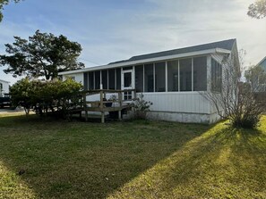 Ein einstöckiges Haus mit überdachter Veranda, einer kleinen Terrasse und einem Rasen.
