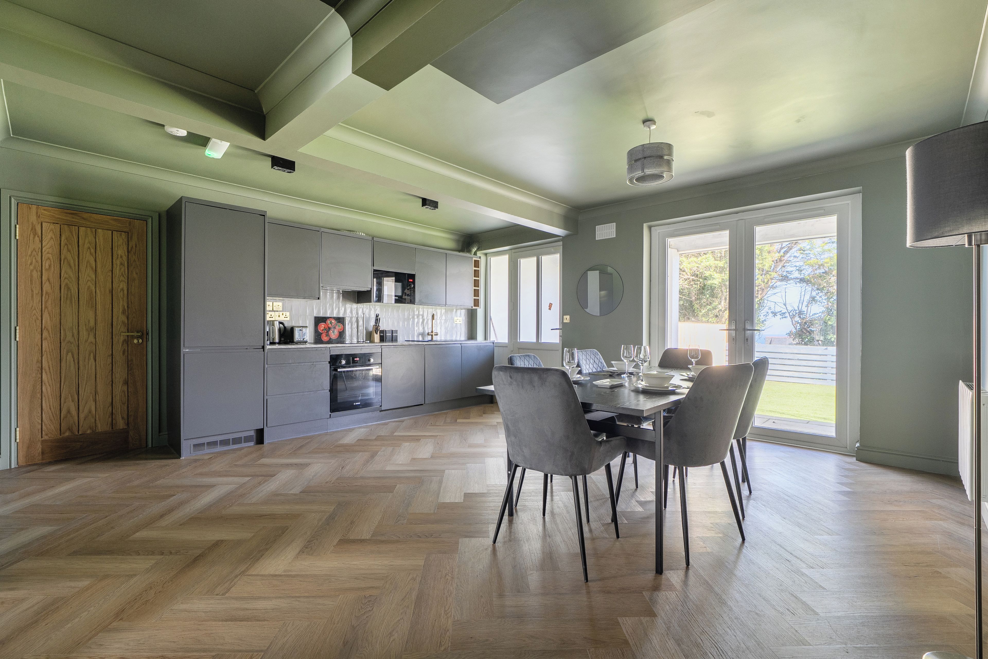 A spacious kitchen with modern appliances, a dining area with a table set for two, and large windows offering a view of the outdoors.