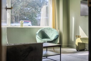 Ein Zimmer mit Fenster, Stuhl, Tisch und Heizkörper.