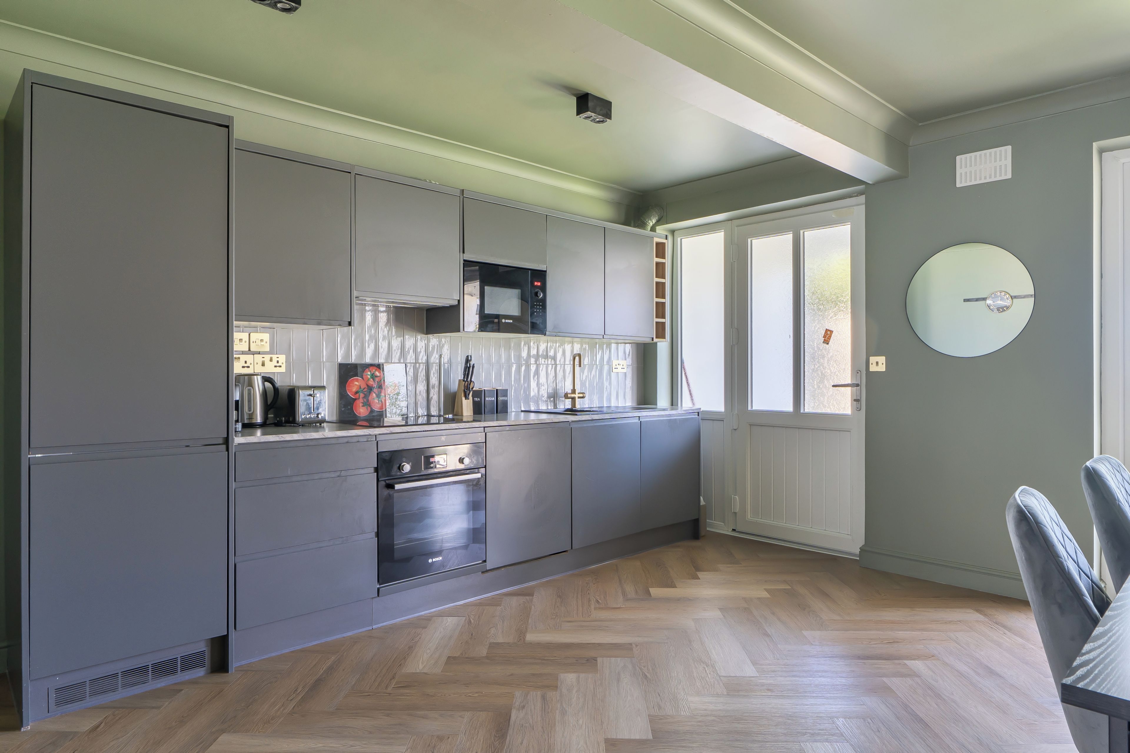 Une cuisine moderne avec des meubles de couleur grise, un four Bosch et une fenêtre à vitrage dépoli.