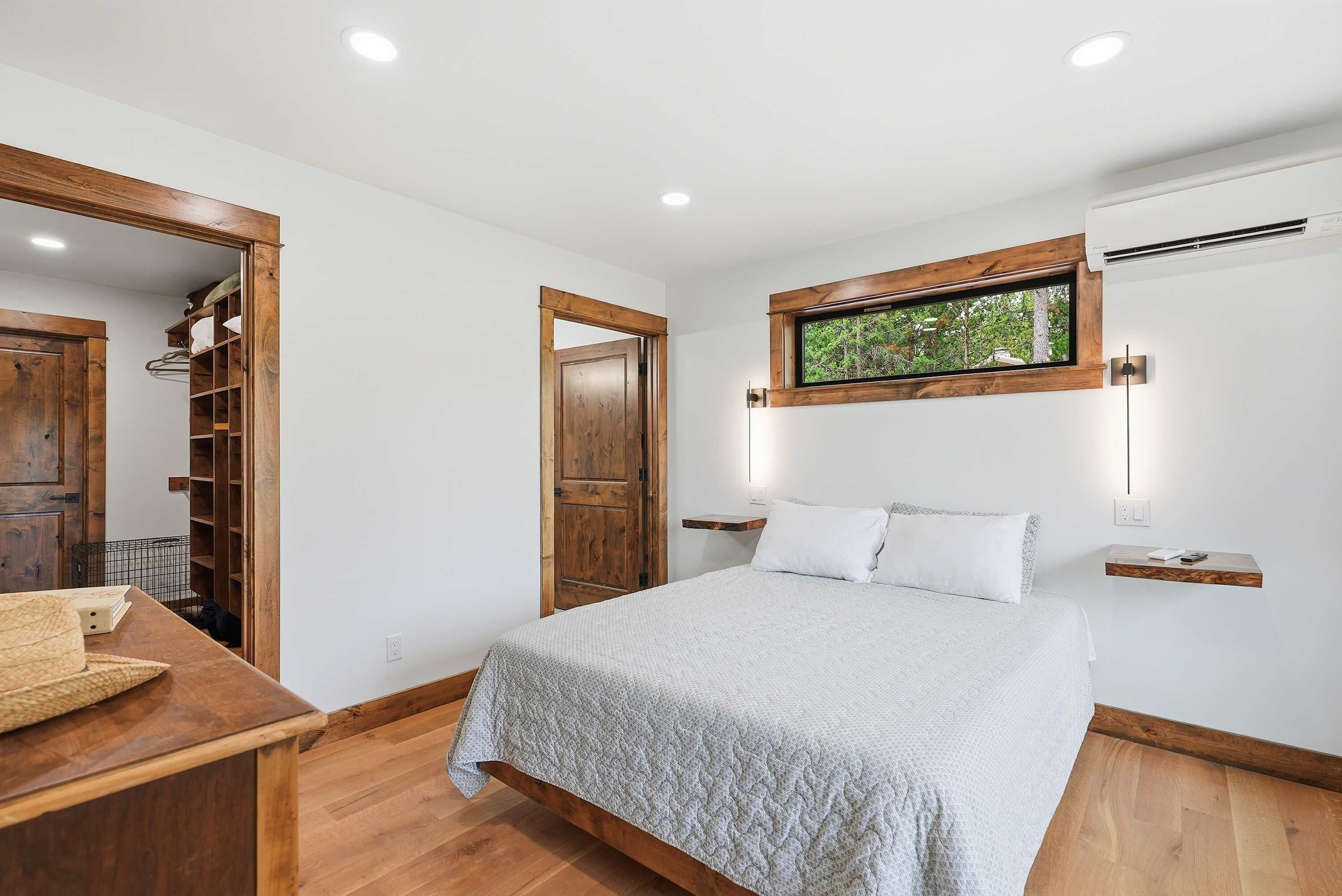 A bedroom with a wooden bed, a nightstand, a wardrobe, and a window with a view of greenery.