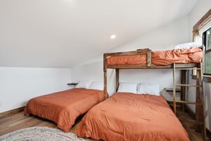 A room with two bunk beds, wooden ladder, white walls, and a window.