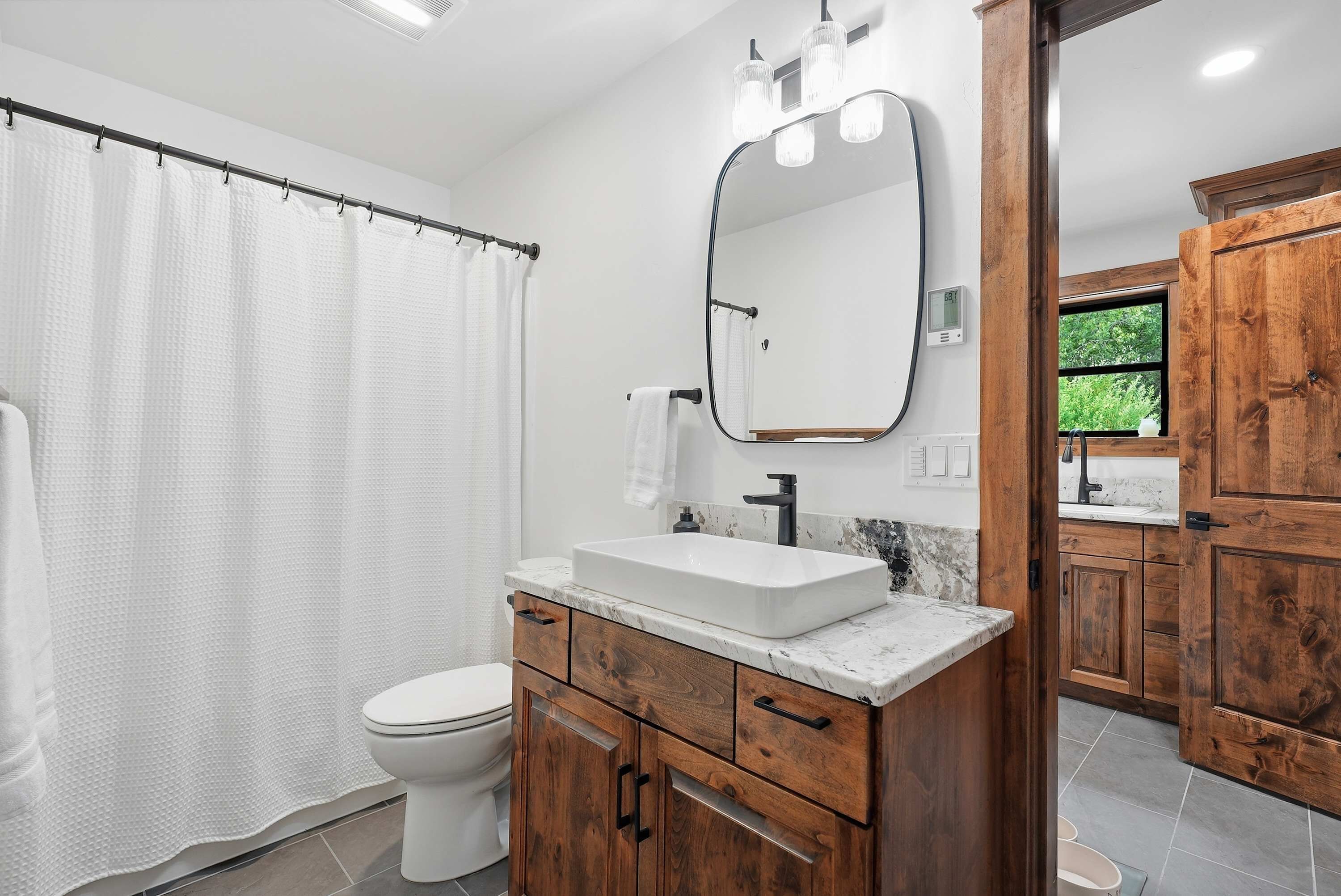 Une salle de bain avec un rideau de douche, des toilettes, un meuble-lavabo avec un évier, un miroir et des armoires en bois.