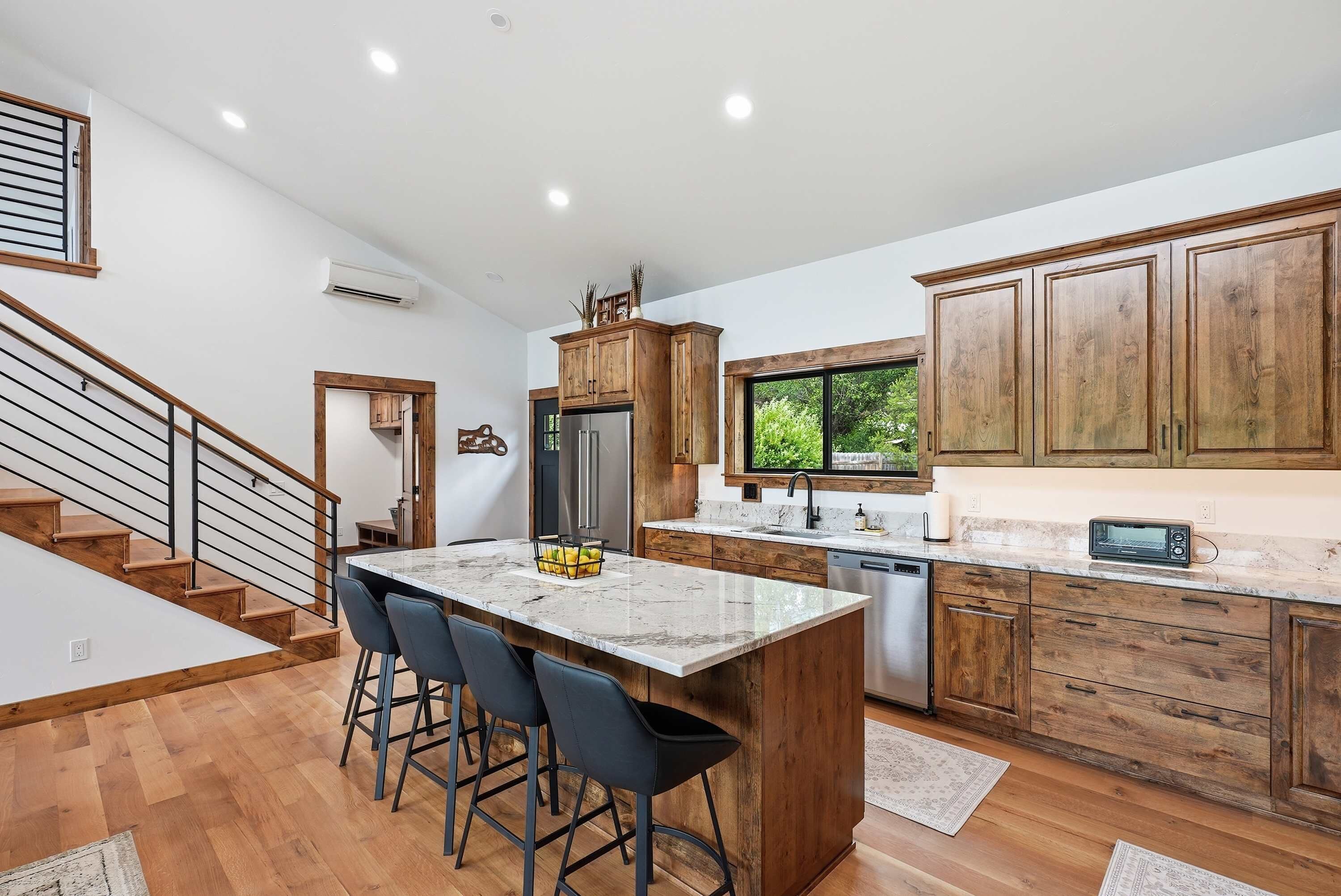 A modern kitchen with a marble island, wooden cabinets, and a stainless steel refrigerator.