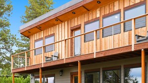 A multi-story wooden building with large windows, a balcony, and a visible staircase. - Big Sunsets on Little Deschutes - Modern Riverfront (La Pine)