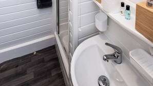 A bathroom with a shower, toilet paper, and toiletries on a shelf. - The Bay Apart-Hotel by Guestz (Morecambe)