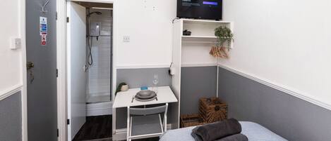 Habitació d'hotel petita amb dutxa, escriptori petit amb cadira, llit, televisió i planta.
