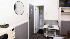 A compact hotel room with a shower, a small table with a bowl and wine glass, a microwave, and a basket of snacks. - The Bay Apart-Hotel by Guestz (Morecambe)