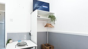 A compact room with a white table set for dining, a small seating area, a television mounted on the wall, and a plant on a shelf. - The Bay Apart-Hotel by Guestz (Morecambe)