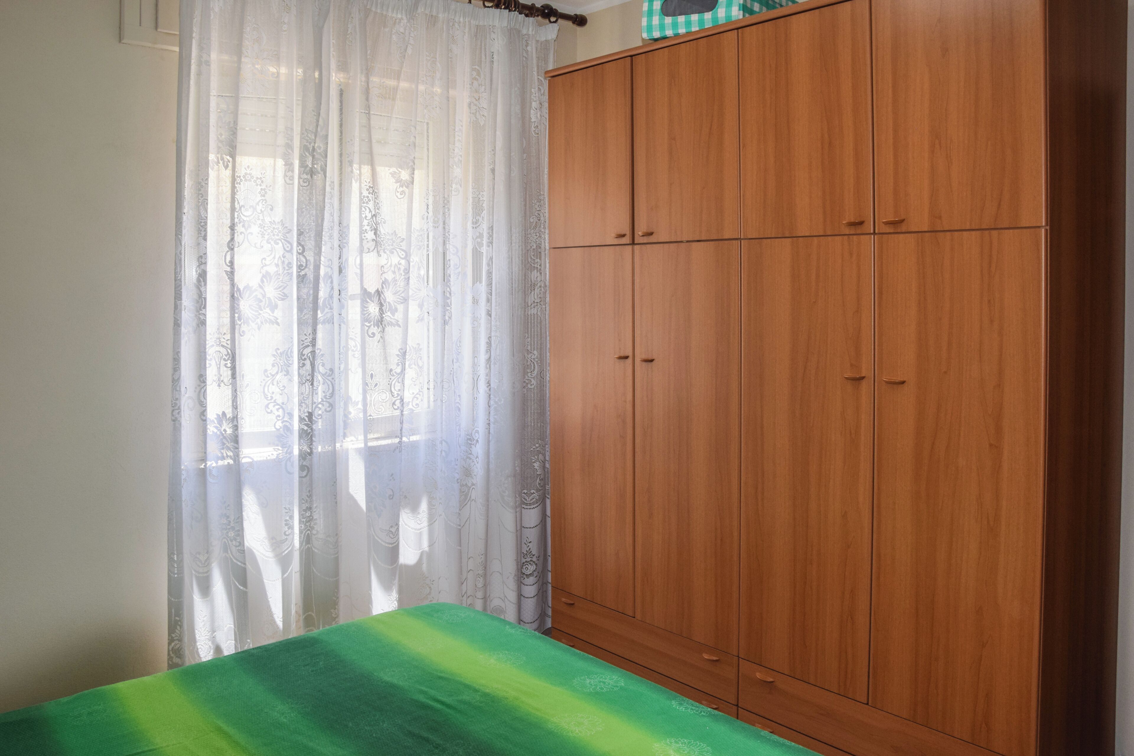 Una habitación con una cama, un armario de madera y cortinas traslúcidas.
