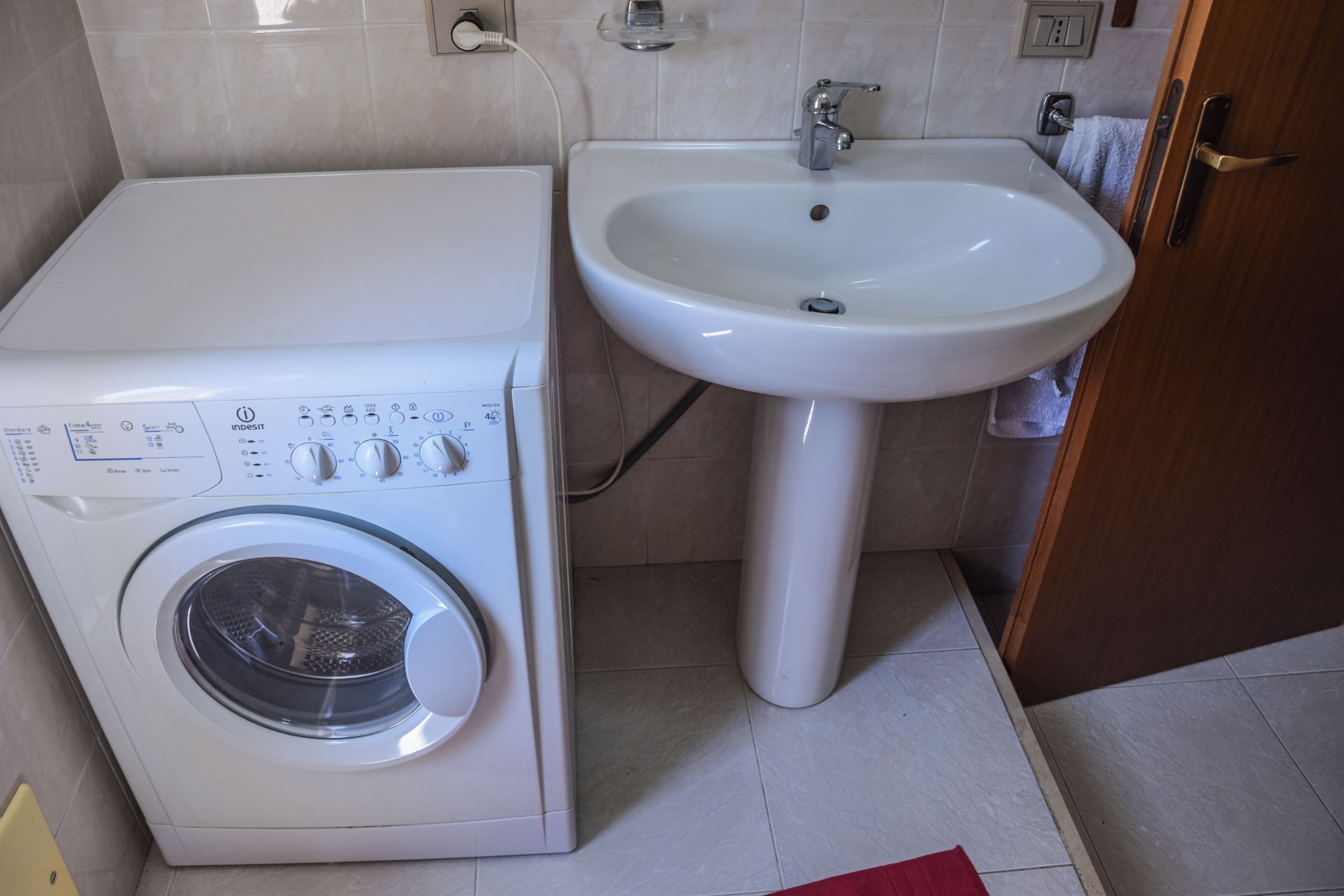 Una lavadora y un lavamanos en un baño con paredes de azulejos y una puerta de madera.