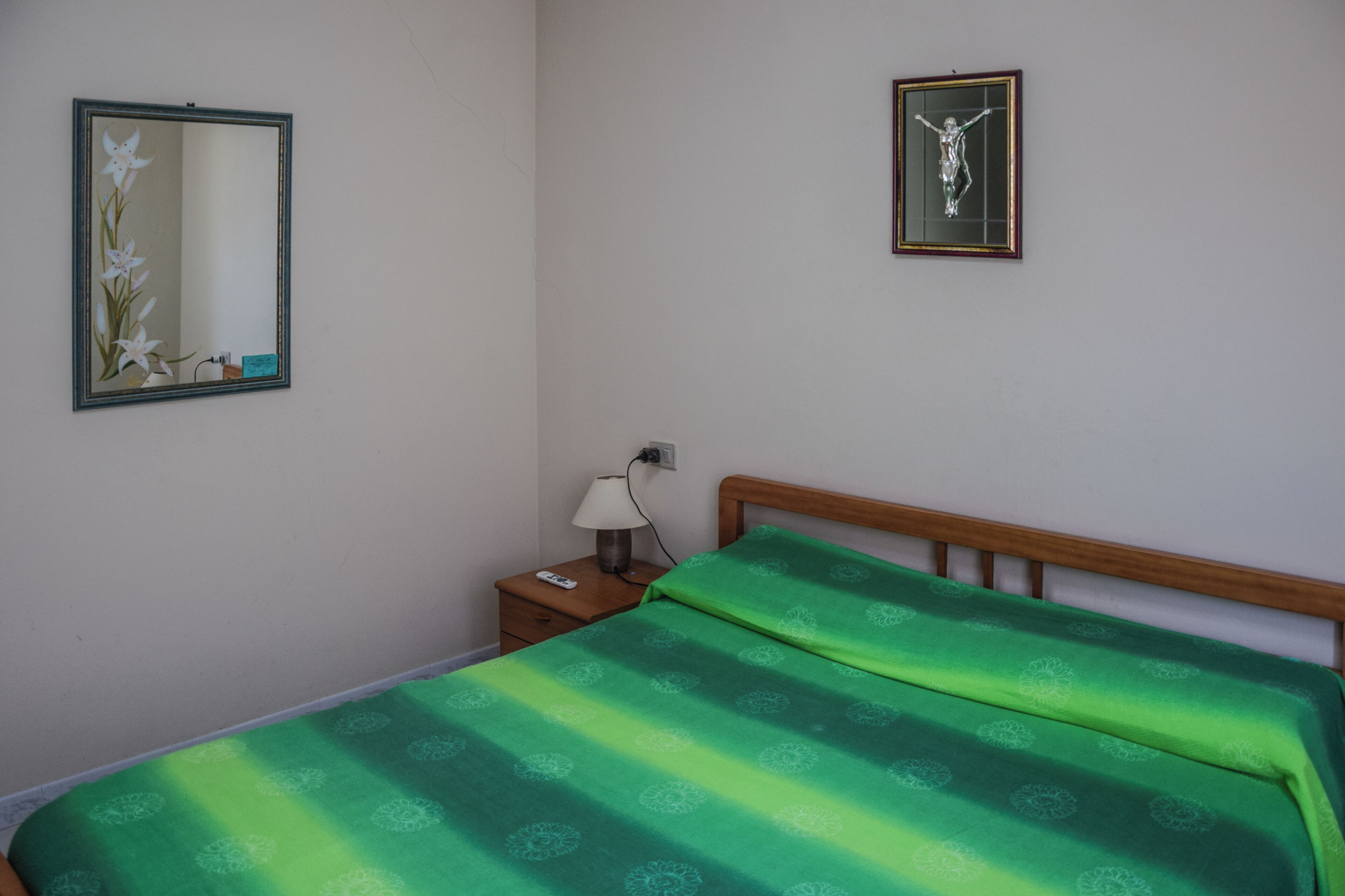 Un dormitorio con una cama, una mesita de noche, una lámpara, un cuadro en la pared y un espejo.