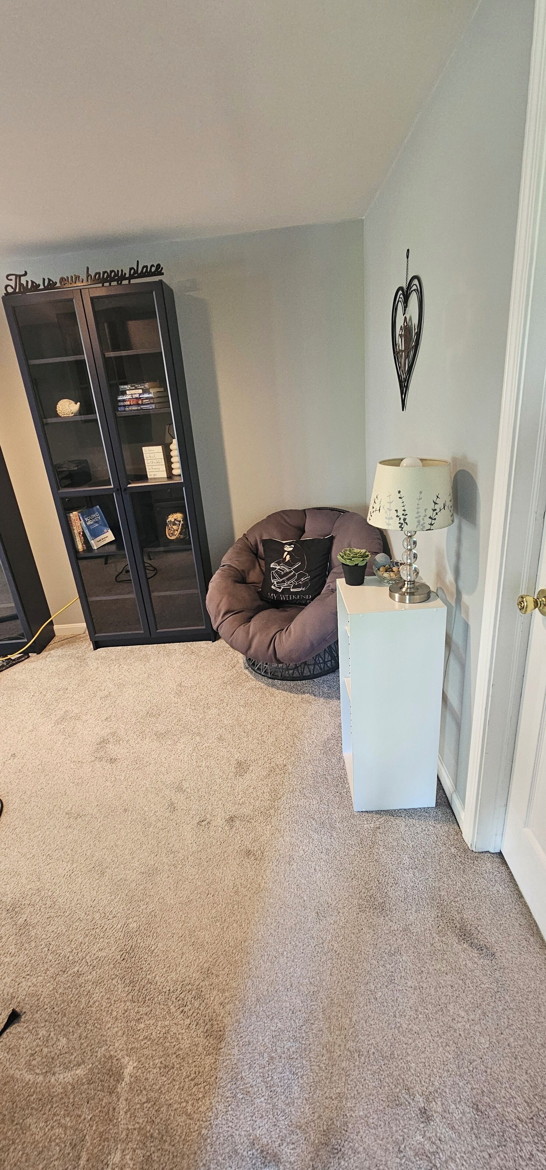 Ein Zimmer mit Bücherregal, einem Sitzsack, einem kleinen weißen Beistelltisch mit Lampe und einer Tür.