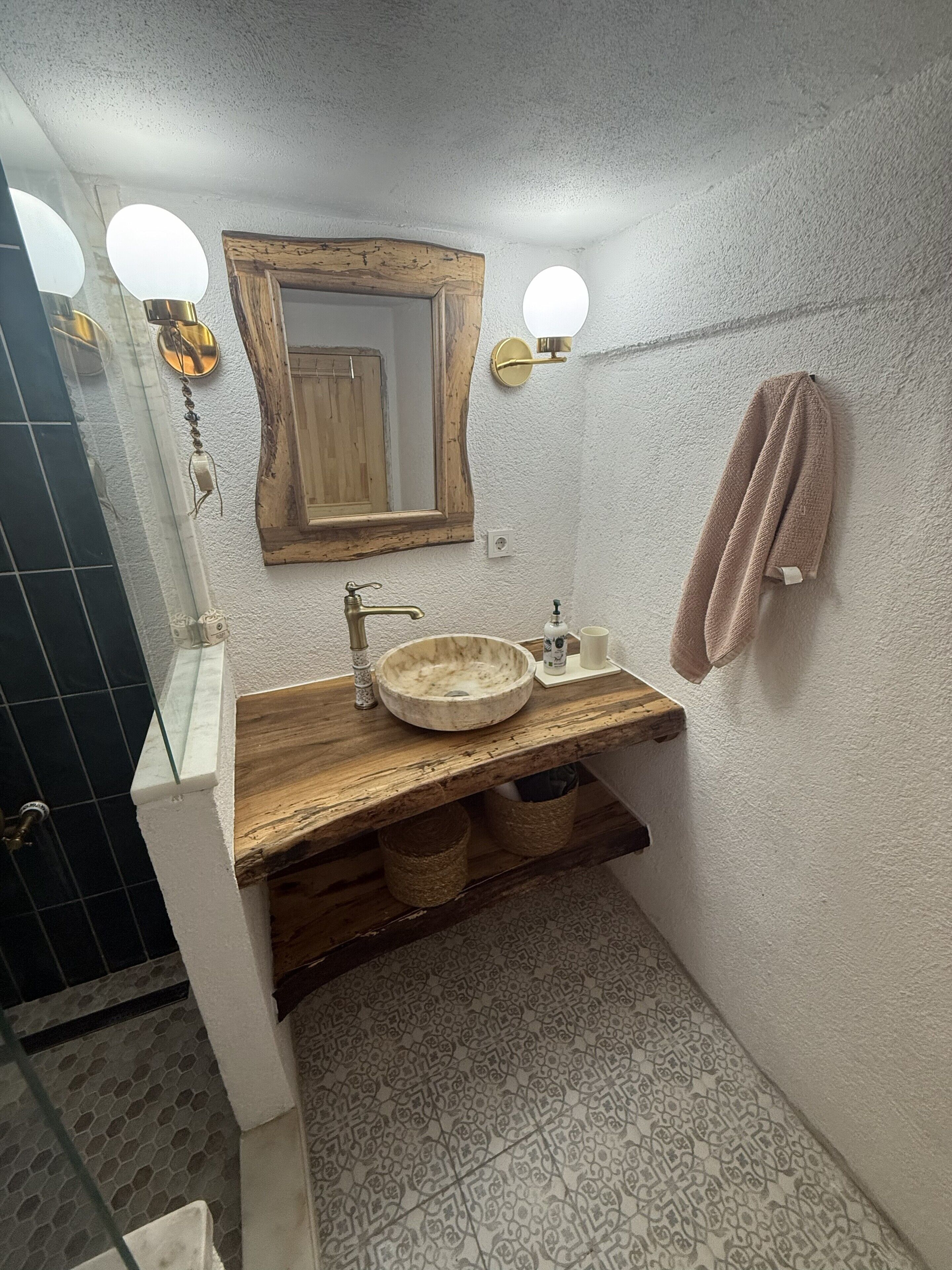 Un baño con tocador de madera, lavamanos de mármol redondo, un espejo grande y una toalla colgada en la pared.