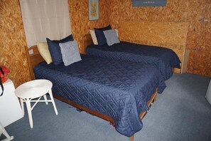 Una habitación con dos camas, una silla blanca pequeña y un escritorio.