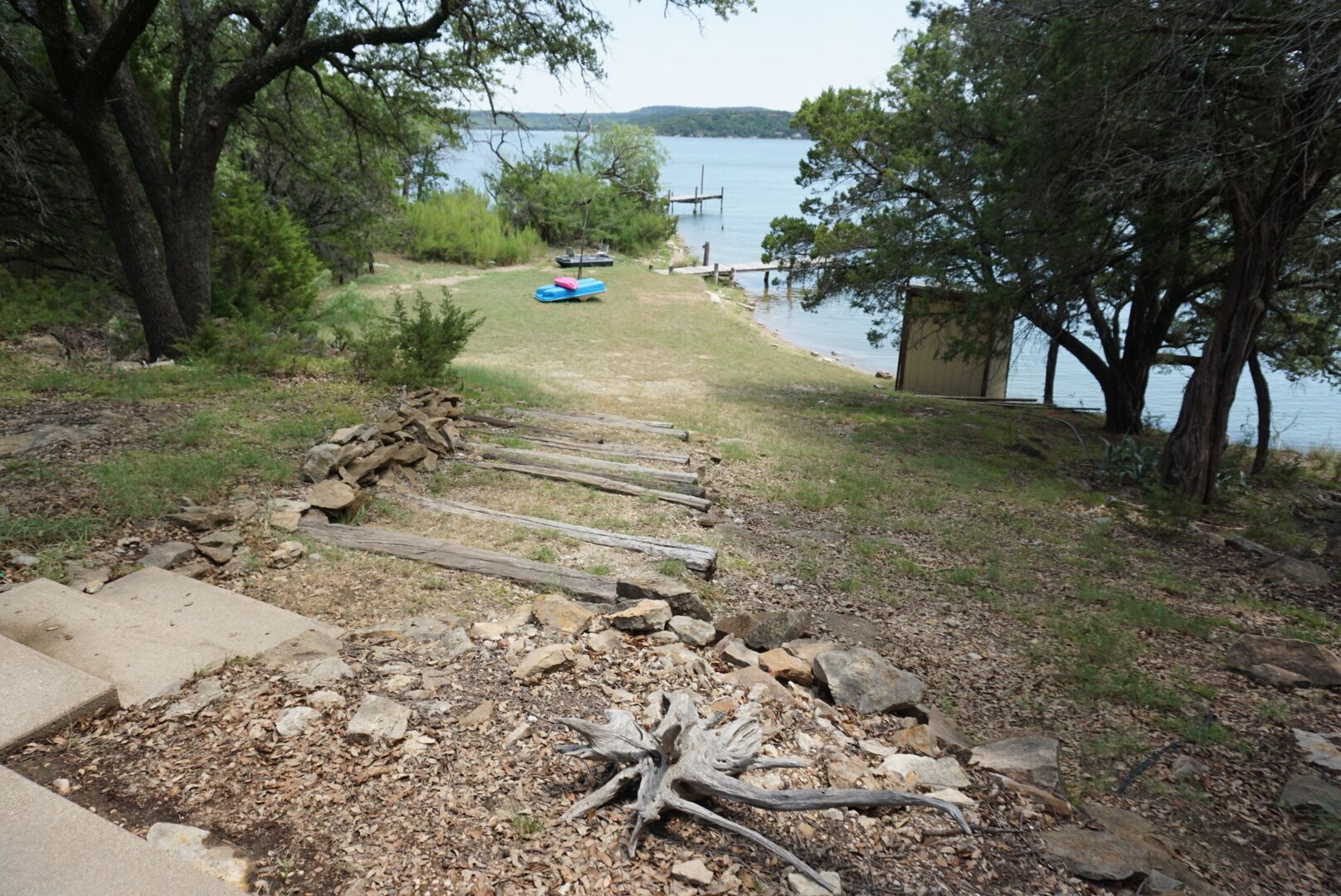 A concrete path leading to a dock by a lake with boats, surrounded by trees and a grassy area.