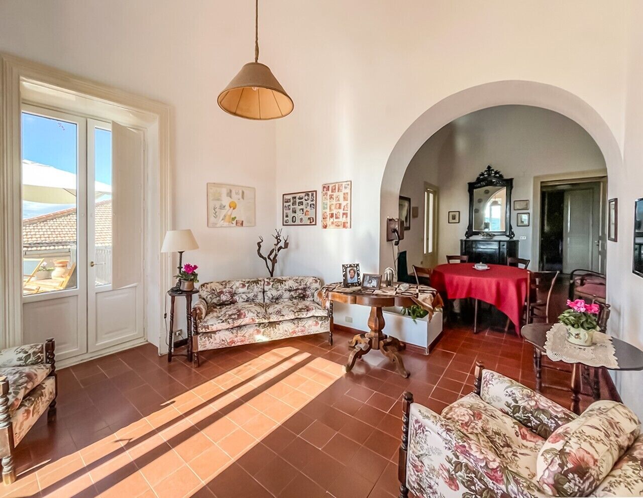 A living room with a sofa, a dining table with chairs, a lamp, and a red tablecloth.