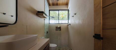 A bathroom with a large sink, toilet, shower, and a window.
