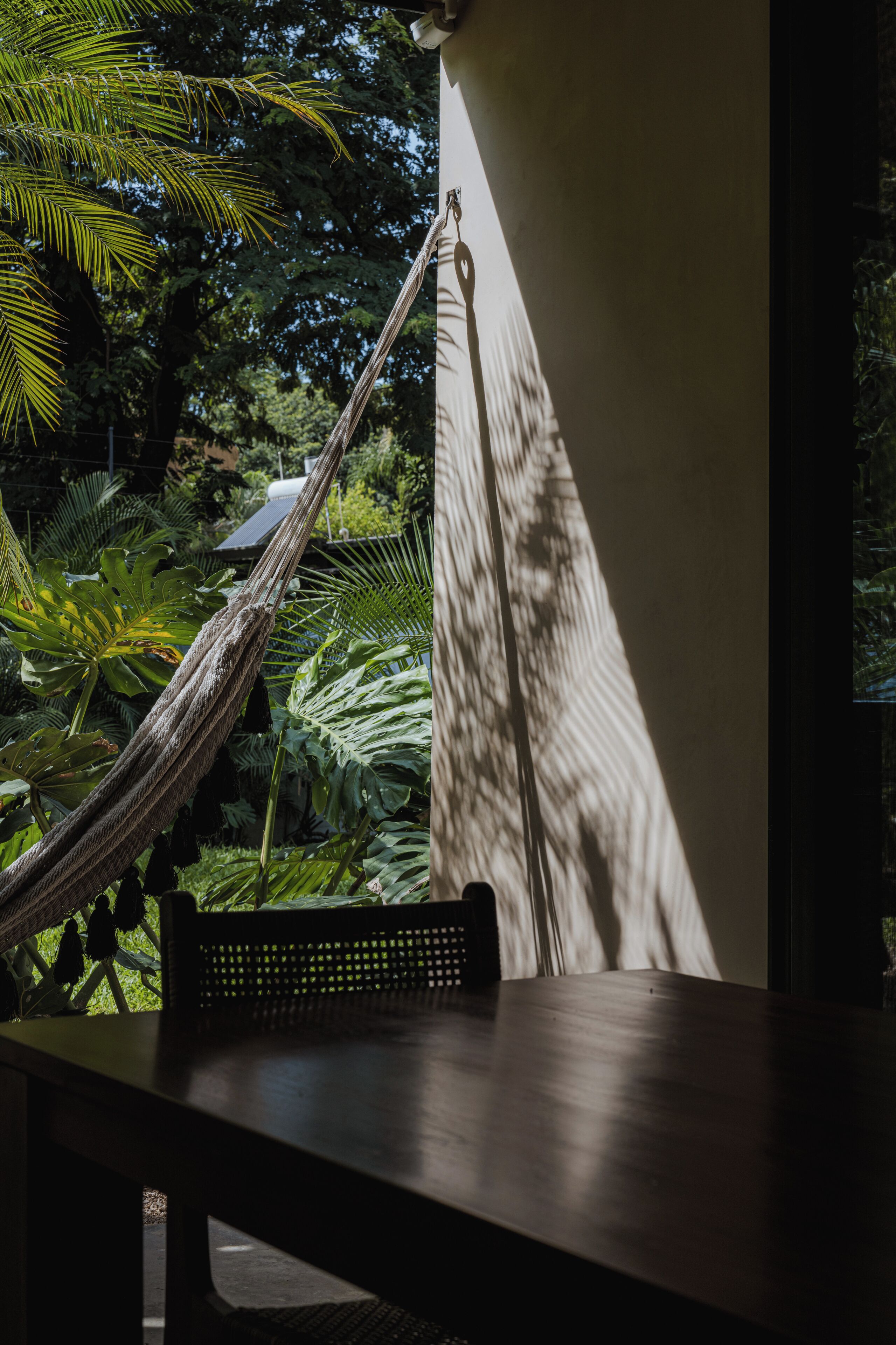 Un hamac est attaché à un mur, une table se trouve à proximité, et un luxuriant décor végétal forme le fond de la scène.