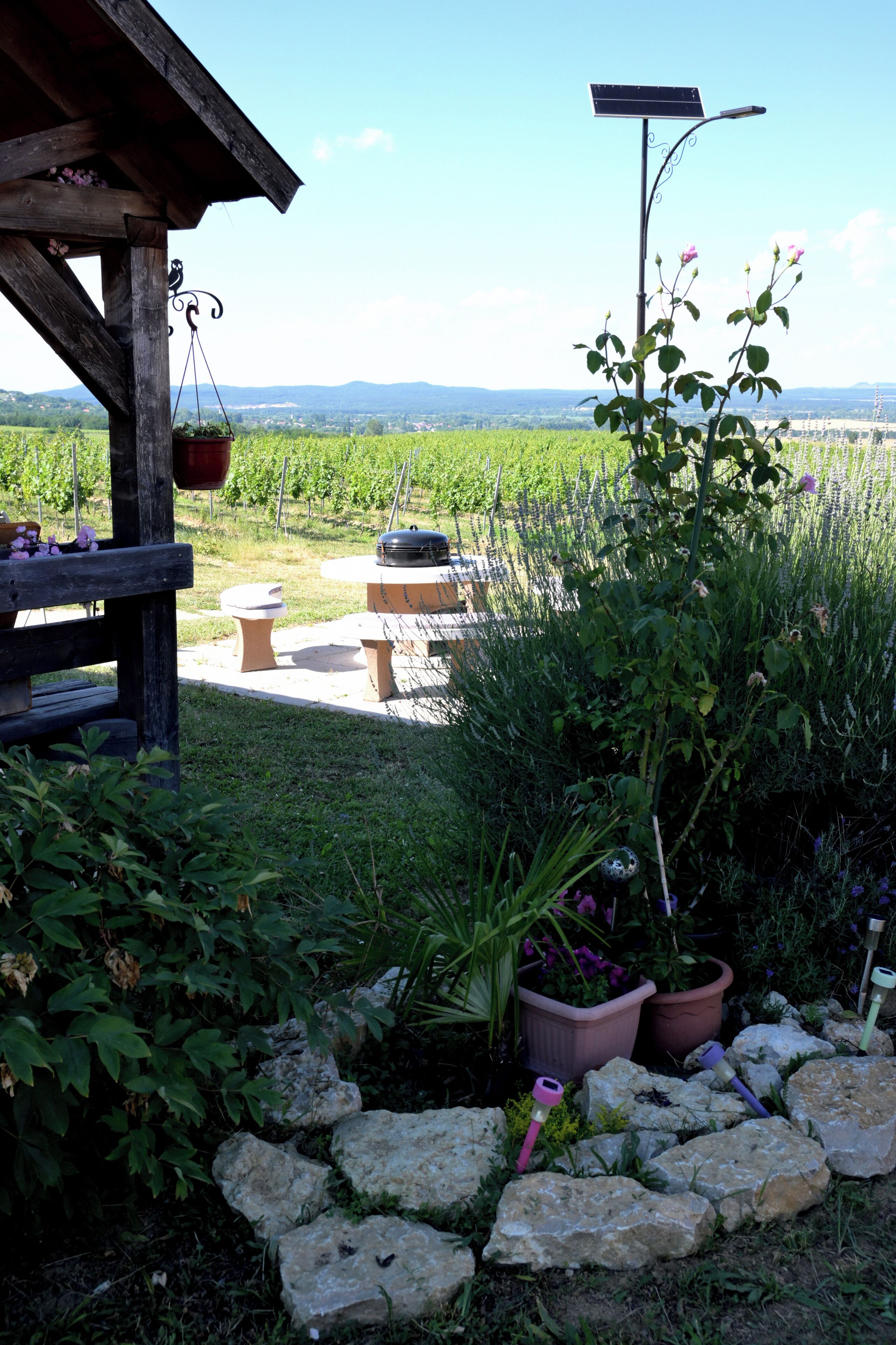 Un espace extérieur aménagé dans un style rustique, avec une pergola en bois, des jardinières en pierre et une lampe alimentée par énergie solaire.