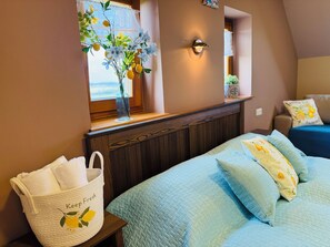 A bedroom with a window, a bedside table, a bed with a quilted bedspread, and a wall-mounted light fixture.