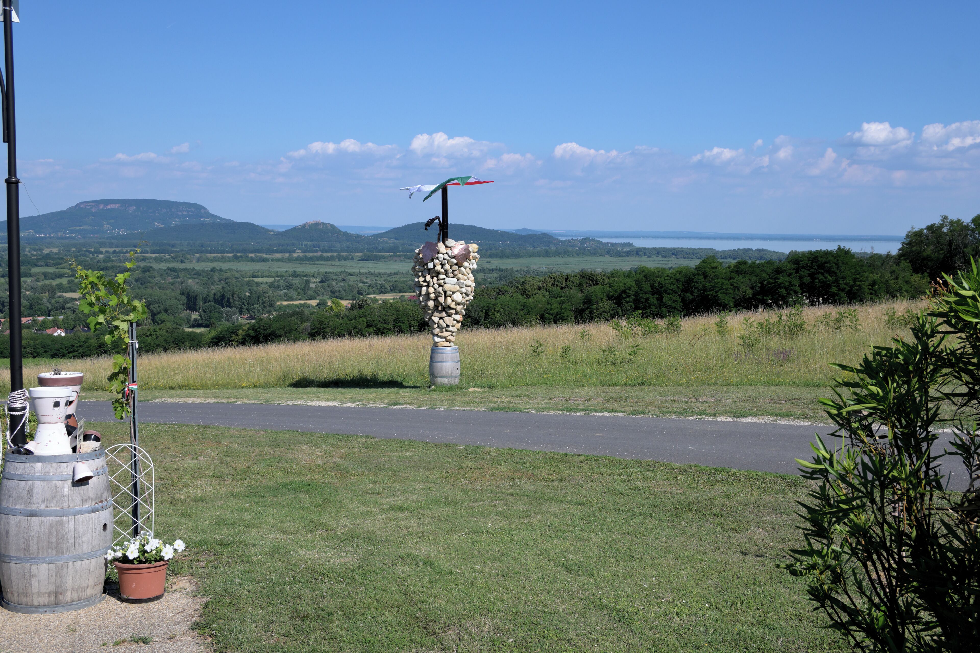 A rural landscape with a road, a bird sculpture on a stone pillar, and potted plants.