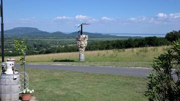 A rural landscape with a road, a bird sculpture on a stone pillar, and potted plants.