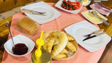 Een tafel met eten, waaronder brood, een mandje croissants, een pot honing en een schaal fruit.