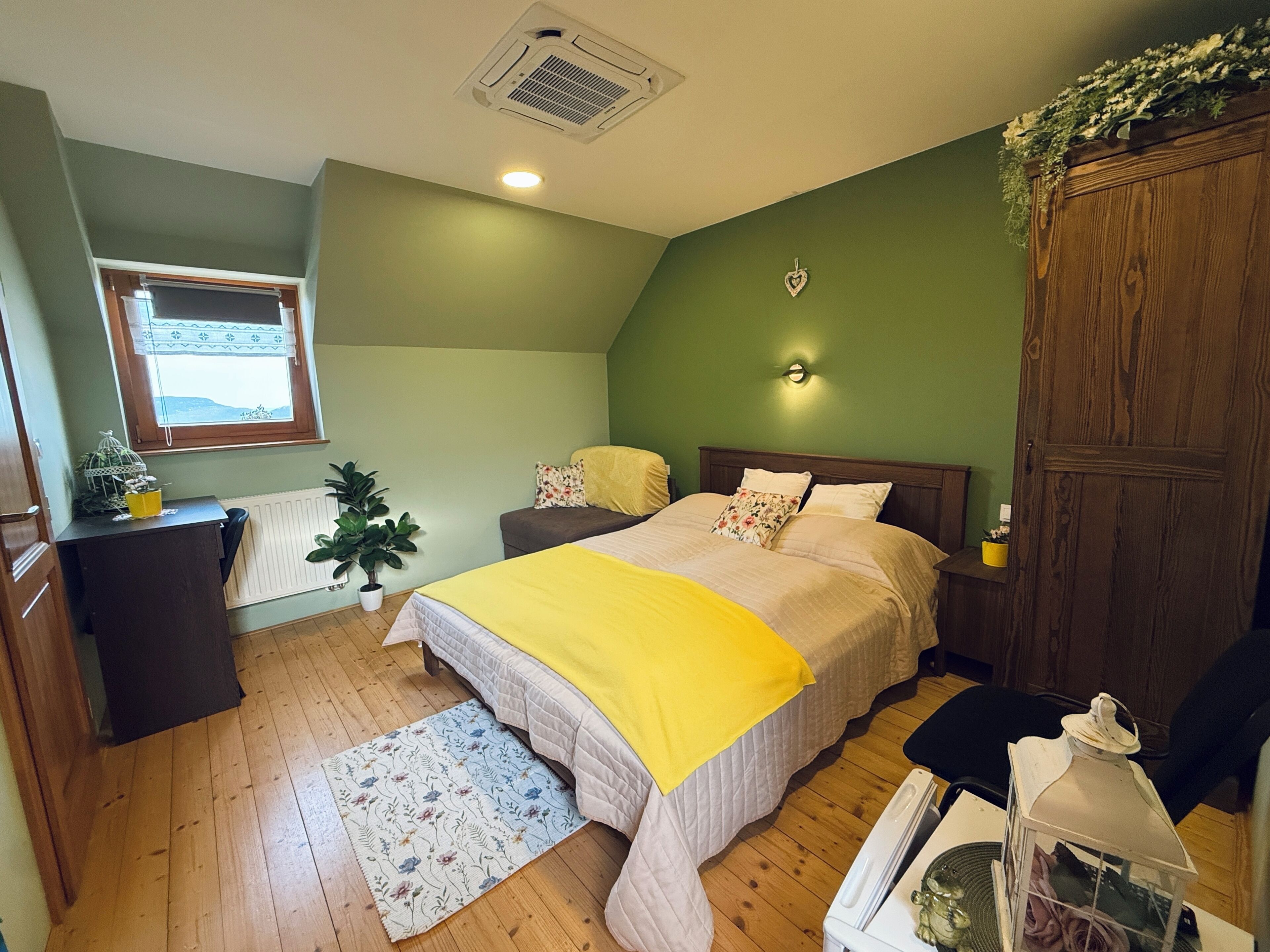 Ein Schlafzimmer mit Bett, Schreibtisch, Heizkörper, Fenster und einer Wandleuchte.