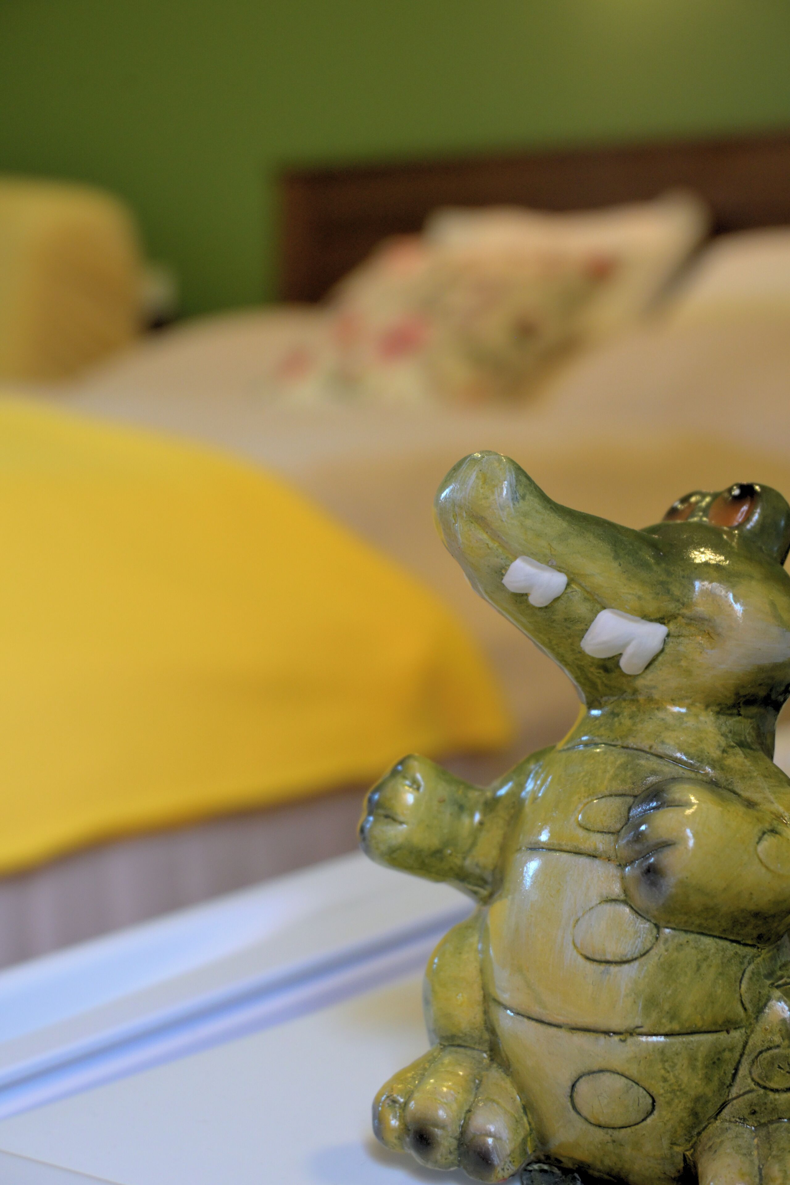 A bed with a yellow pillow and a green and white decorative object resembling a crocodile.