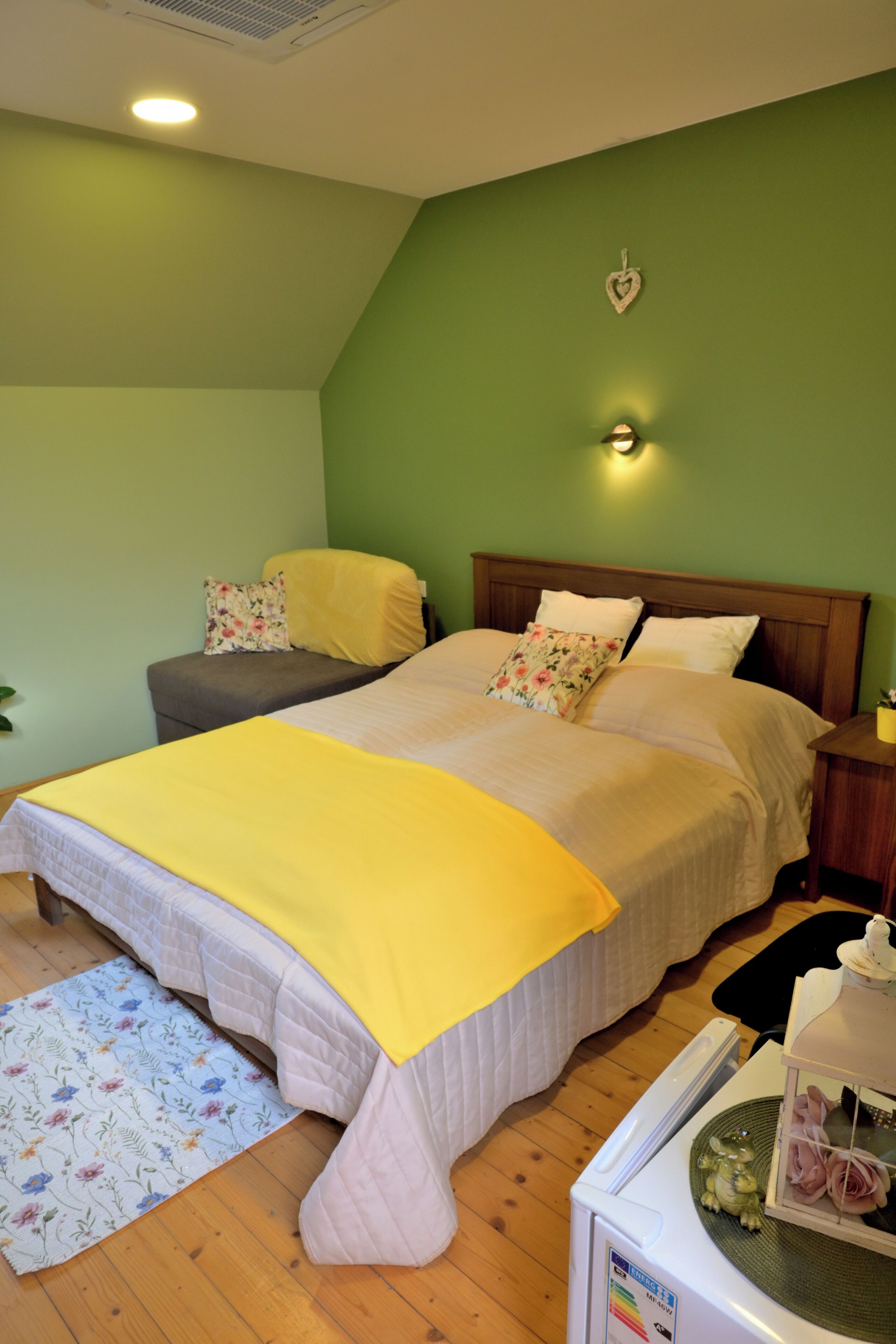 Un dormitorio con una cama, una mesita de noche, una lámpara de pared y una pared verde.