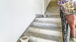 A staircase with a stone floor, a potted plant with dried flowers, and a wall-mounted light fixture.