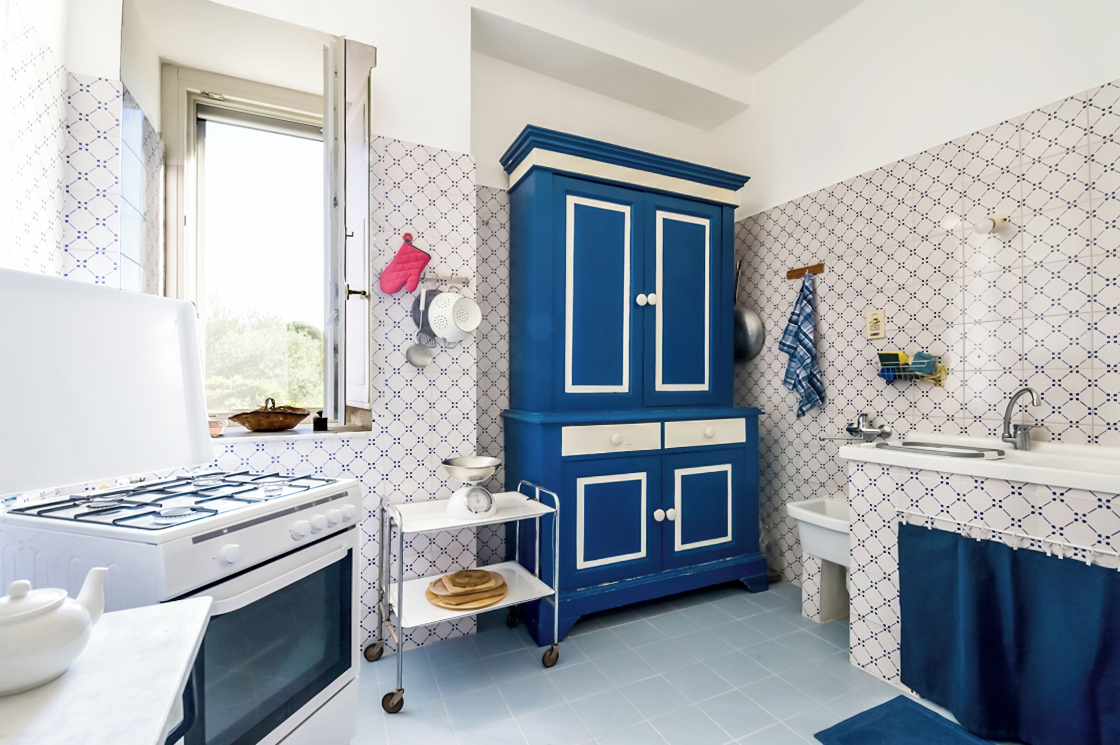 A kitchen with a stove, sink, blue cabinet, and patterned walls.