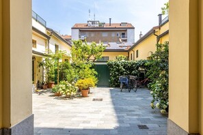 Une cour intérieure agrémentée de plantes en pot, de vélos et d’un portail vert.