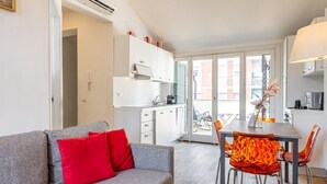 A modern apartment with a grey sofa, red cushions, a dining table with orange chairs, a kitchen, and a balcony with a bicycle. - Luxury Apartment with Terrace - Garibaldi Station (Milan)