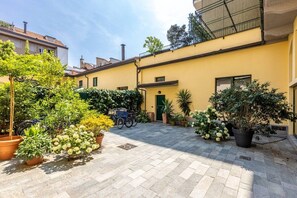 Une cour intérieure agrémentée de plantes en pot, un vélo et un bâtiment à la façade jaune.