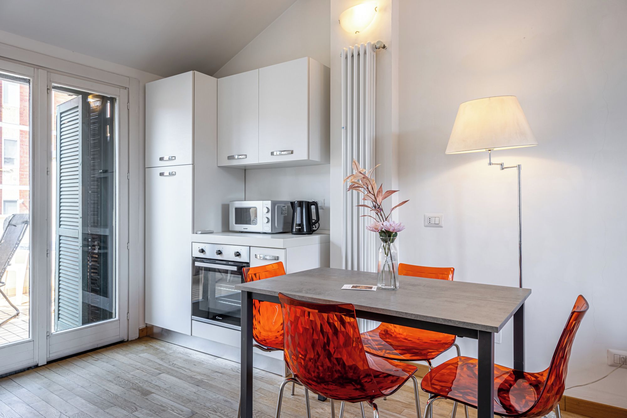 Een moderne keuken met witte kasten, een magnetron, een waterkoker en een tafel met oranje stoelen.