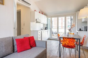 A modern apartment with a grey sofa, red cushions, a dining table with orange chairs, a kitchen area, and a view through a glass door. - Luxury Apartment with Terrace - Garibaldi Station (Milan)