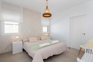 Ein Schlafzimmer mit Bett, Nachttischen, einer Hängeleuchte, einem Fenster und einer Tür.