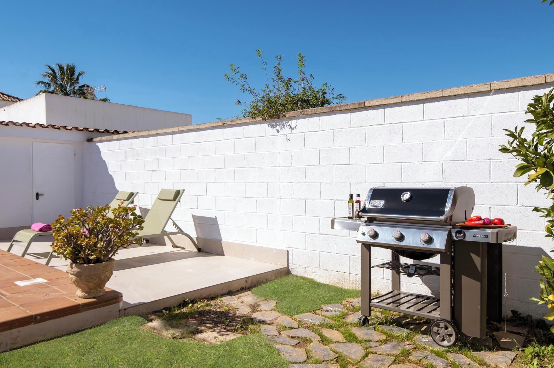 Eine Terrasse mit Grill, Sitzgelegenheit im Freien und einer weißen Ziegelwand.